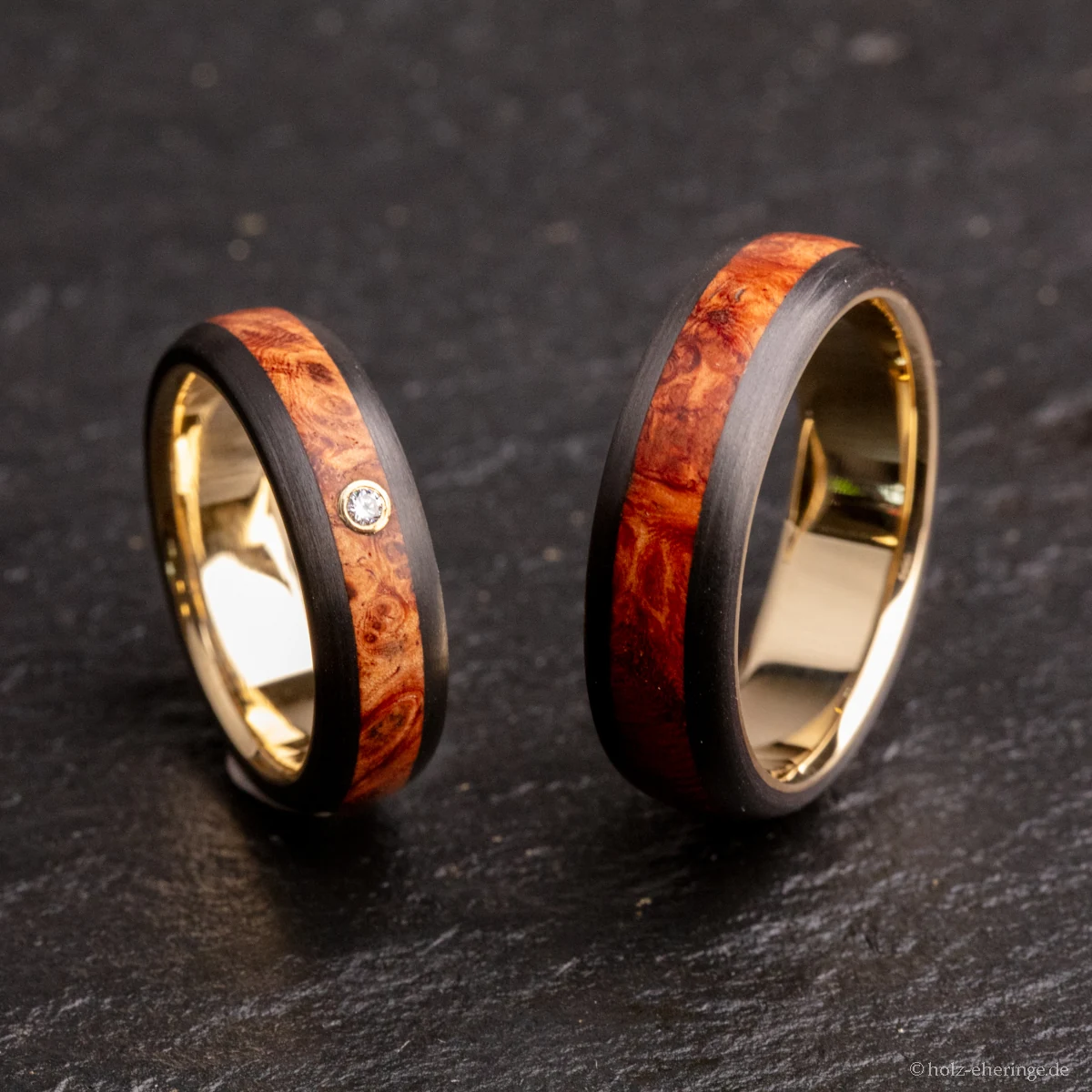 Zwei aufrecht stehende CrownDesign-Ringe aus Carbon mit Holz-Inlay und goldfarbenen Innenringen