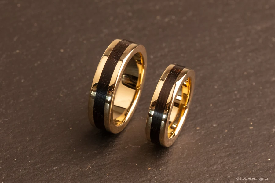 Zwei CrownDesign-Ringe mit goldfarbenen Kanten und dunklem Mooreiche-Inlay auf einer Steinplatte